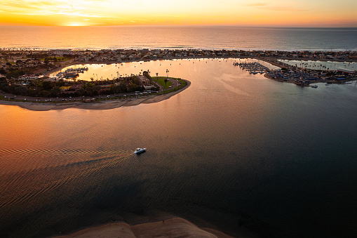 Experience the enchanting beauty of Mission Bay in San Diego, California, as the sun dips below the horizon, merging with the water in a breathtaking sunset. In the tranquil waters, a solitary boat gracefully glides, creating a scene of serene coastal elegance