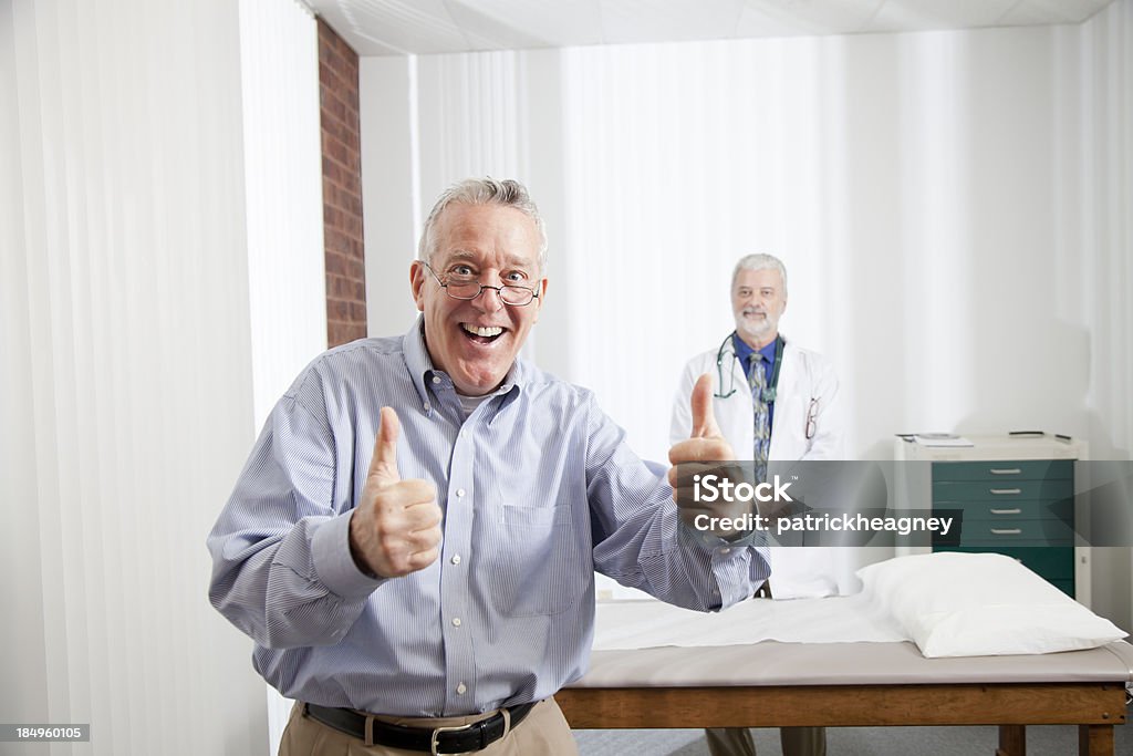 Улыбающаяся пациент дает большие пальцы вверх с врачом в фоне - Стоковые фото Юмор роялти-фри