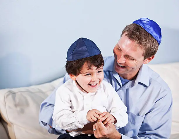 Jewish father (30s) and son (3 years) sitting together, laughing.