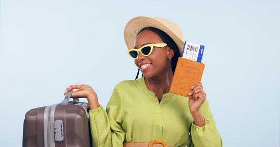 Happy African woman, passport and studio with suitcase, airplane ticket and documents by blue background. Girl, legal paperwork and luggage for compliance, vacation and sunglasses for global travel