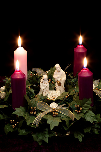 Christmas Advent wreath with Nativity scene in middle of four burning candles and holly. Vertical image would be good for Christian or religious Christmas use.