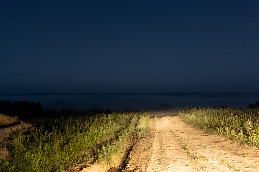 dry dirt road in the middle of nowhere lit with car headlights at early foggy morning