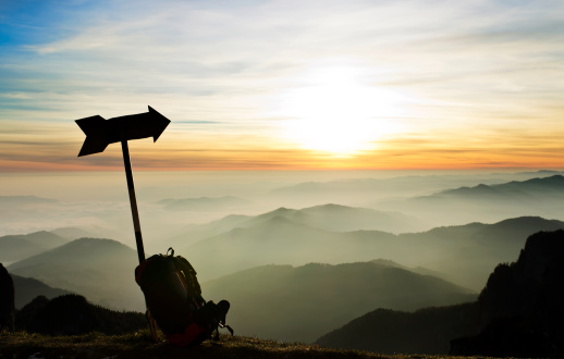 hiking trail directional sign and backpack in front of majestic sunset