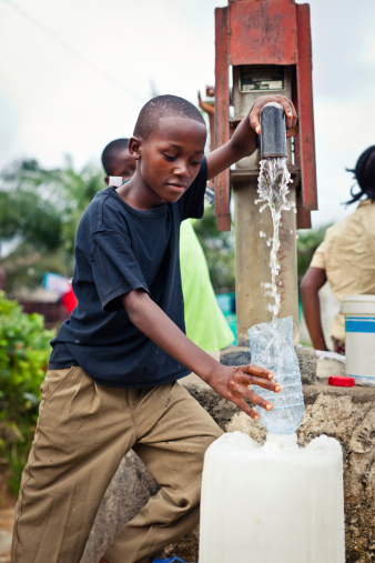 An African boy holding a water bottle funnel while clean water pours into the bucket.