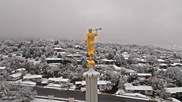 Drone circles around golden angel with trumpet with snow covered neighborhood behind