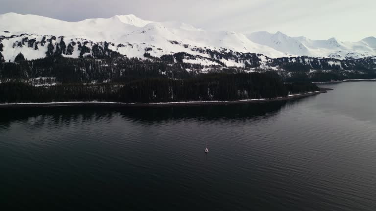 Drone shot of a sailboat in front of snowy mountains of Montague Island, Alaska