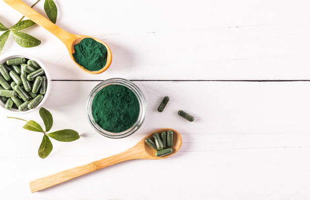 Green powder and spirulina algae tablets in glass jars and spoon on white wooden background. Top view. A copy space. high content of multivitamins. Green powder and spirulina algae tablets in glass jars and spoon on white wooden background. Top view. A copy space. high content of multivitamins chlorella stock pictures, royalty-free photos & images