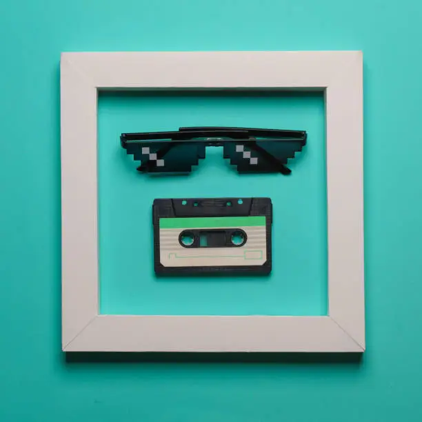 Photo of Pixel sunglasses and audio cassette in white frame on blue background. Creative layout. Minimalism