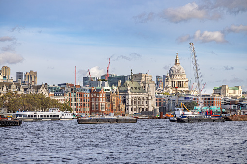 South bank of river Thames, London, England - October 27th 2023:  View over river Thames to St Paul's Cathedral surrounded by construction sites and with a nautical vessel in the front