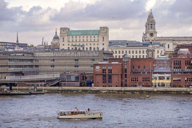 South bank of river Thames, London, England - October 28th 2023:  Examples of old and new buildings at the side of the river Thames with a veteran boat in front