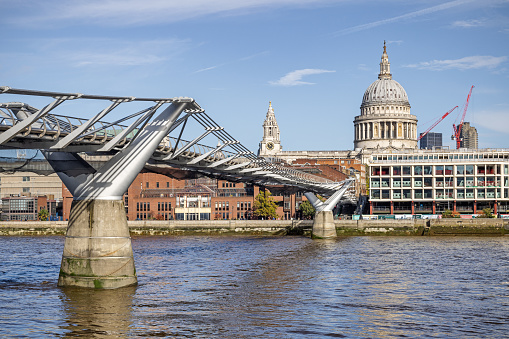 South bank of river Thames, London, England - October 28th 2023:  The Millennium pedestrian bridge with St Paul's Cathedral surrounded by construction cranes behind