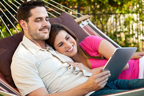 Tablet Computing In A Hammock XXXL.  Young couple using a tablet computer while relaxing in a hammock. hammock men lying down digital tablet stock pictures, royalty-free photos & images