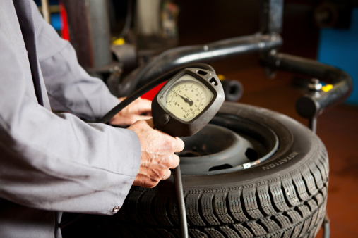 In auto repair shop...Ccar mechanic is checking tire air pressure