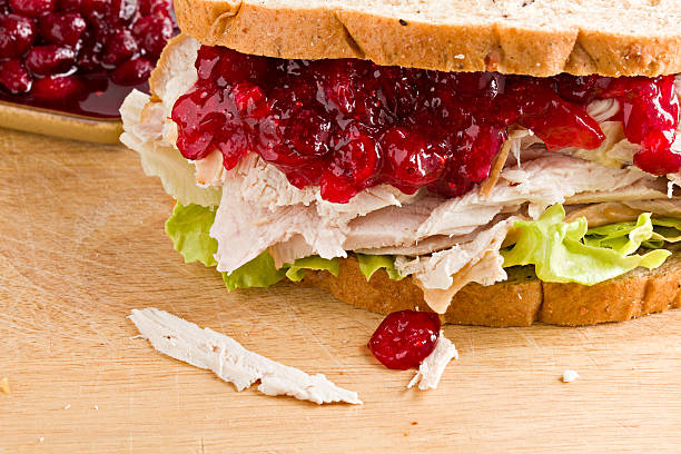 Turkey And Cranberry Sandwich A close up of a turkey and cranberry sandwich sitting on a wooden cutting board with a small brown bowl of homemade cranberry sauce in the background. leftovers photos stock pictures, royalty-free photos & images