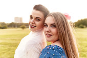 Happy lovely bride in white dress with white veil and blond bridesmaid in summer park. Young charming girls smile and hug. Cheerful bachelorette party. Close-up portrait.