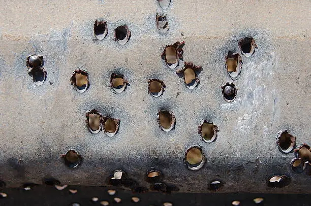 These holes are result of a Hizbullah missile landing in Haifa, Israel in the summer of 2006.  Upon impact, the missile exploded, throwing small metal balls up to 1 km away.  This traffic railing was near the impact zone, and as a result, suffered much damage.  Two pieces of shrapnel are lodged into the metal.