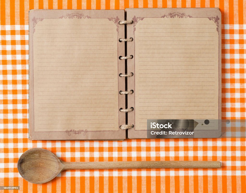 Antique notebook and wooden spoon on orange tablecloth Wooden spoon and old notebook on orange tableclot. Cookbook Stock Photo
