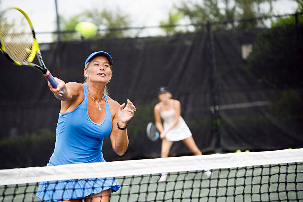 Womens doubles match tennis volley Mature woman hitting a forehand winner in doubles match. tennis senior adult adult mature adult stock pictures, royalty-free photos & images