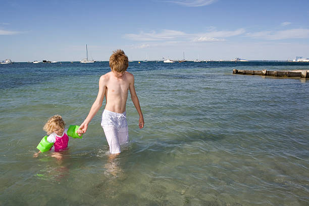 A teenager supervising a three year old at beach.
