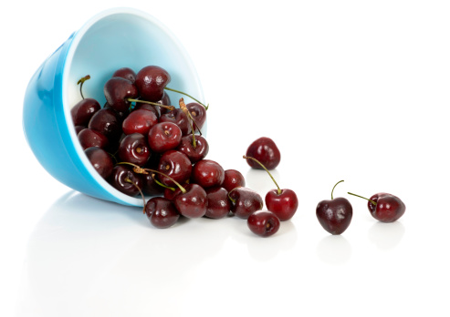 Cherries spill from a bowl on white.