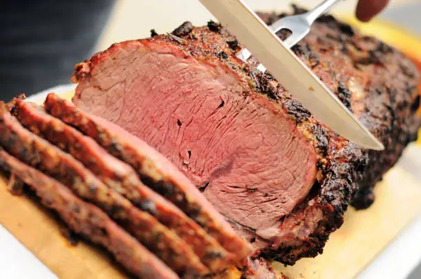 "Beautiful prime rib (standing rib) roast being sliced. Crusted with garlic, rosemary and horseradish. Cooked on a barbeque."
