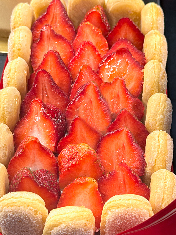 Stock photo showing close-up, elevated view of French patisserie strawberry  Charlotte Russe made by lining a mould with sponge lady's fingers, filing with Bavarian cream (custard) and topping with strawberry halves, on sale in a glass bakery display.