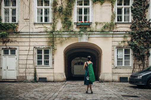 Young woman musician with violin case standing on the street in Vienna and looking at building.