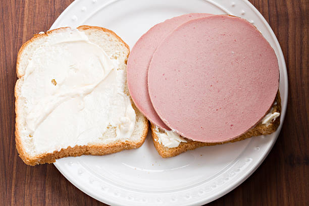 Bologna Sandwich An overhead close up view of a white plate with an open face bologna sandwich on white sourdough bread. baloney photos stock pictures, royalty-free photos & images