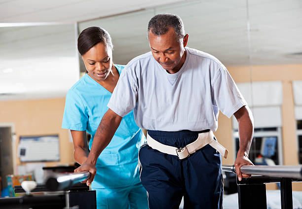 Therapist with patient doing gait training A female physical therapist assists an older male patient while doing gait training.  The man is holding on to railings, while the woman is behind him. occupational therapy photos stock pictures, royalty-free photos & images