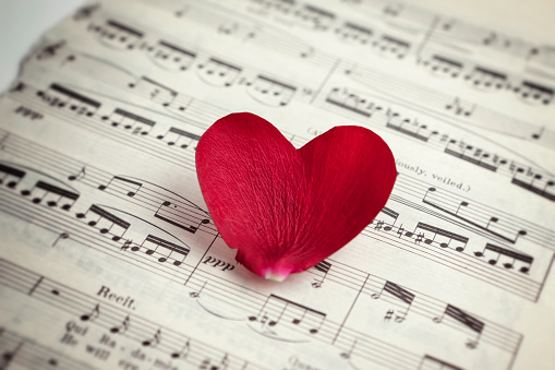 Heart shaped rose petal on music sheet. Love song concept. Music sheet is vintage from Aida by Giuseppe Verdi.