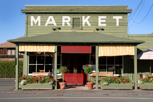 Small town America, country market store and cafe in Yountville, Napa Valley, California, USA. Exterior of an old-fashioned rural retail shop building, painted green with yellow striped awnings and flower boxes, under a clear blue summer sky.