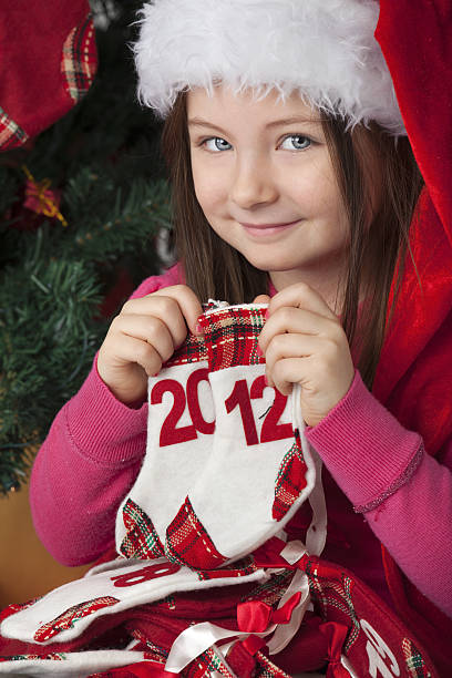 Santa hat wearing Little Girl holding 2012 date "Blue eyes girl, on tree background.Holding a sock." christmas child cheesy grin toothless smile stock pictures, royalty-free photos & images