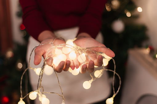 Young woman in a red Christmas sweater holds a golden light garland with golden Christmas lights on the background, Christmas Festival, New Year Festival