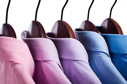 Close-up of pink and blue button down shirts hanging on hangers arranged in a row.
