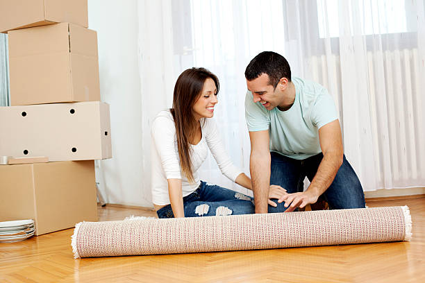 istock Couple Moving to new house - unrolling carpet 184982555