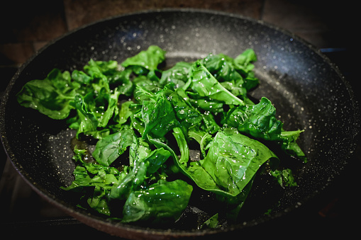 close up of preparing spinach in frying pan.