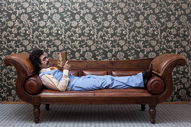 istock Adult man lying down on sofa and reading book 184985568