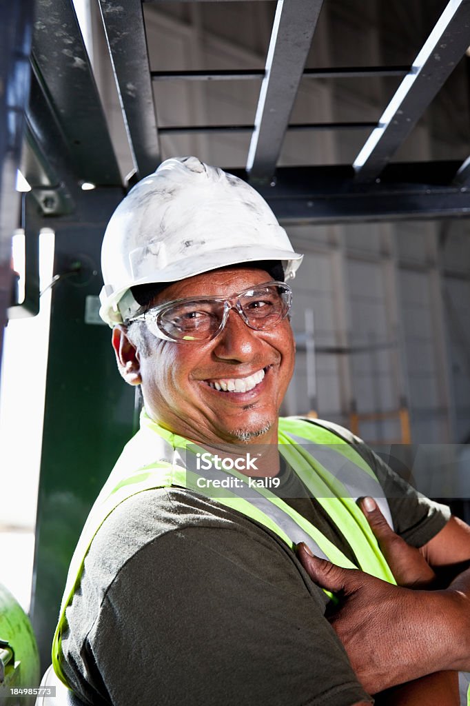 Close up of manual worker Hispanic workman, 40s, in hard hat and safety glasses. Manufacturing Occupation Stock Photo