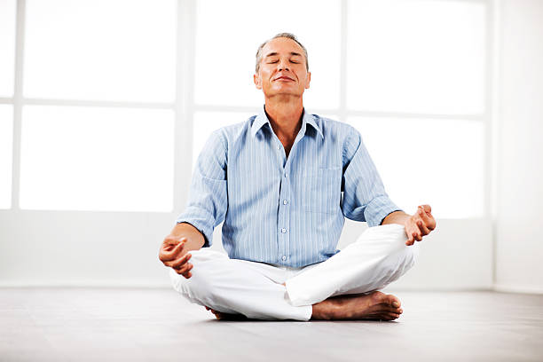 Full length of a healthy young man meditating in lotus position on exercise mat. Vertical shot. Isolated on white.