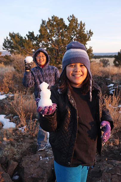 Little girl in the foreground with a boy in the background playing with snow.