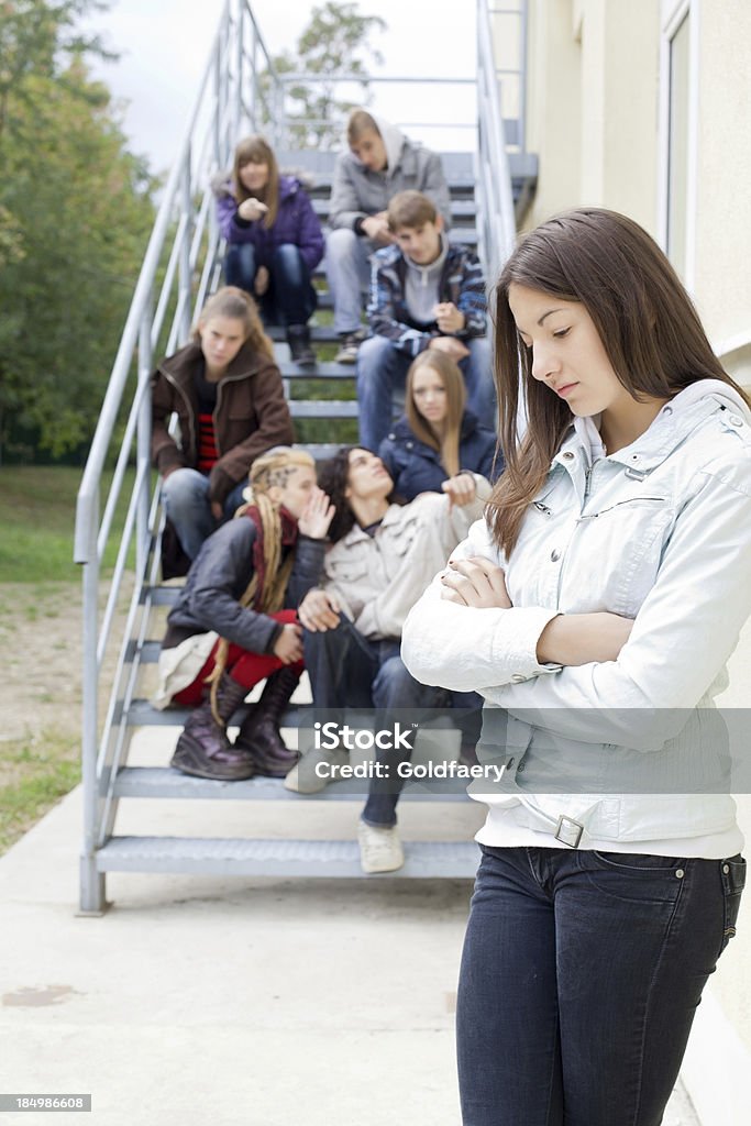 Descontente adolescente e seus colegas de turma gossiping no plano de fundo. - Foto de stock de Calúnia royalty-free