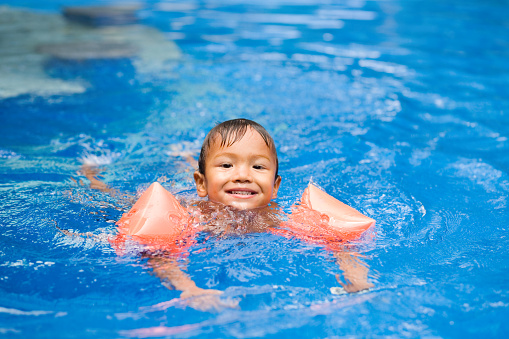 Child 2 years old half asian half caucasian swimming with water wings in pool