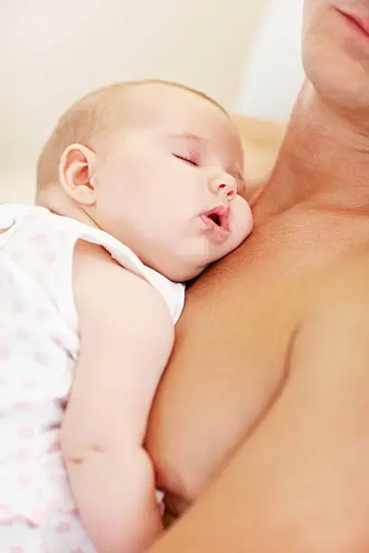 Closeup of a slumbering baby girl being cradled upon her fathers chest on the sofa