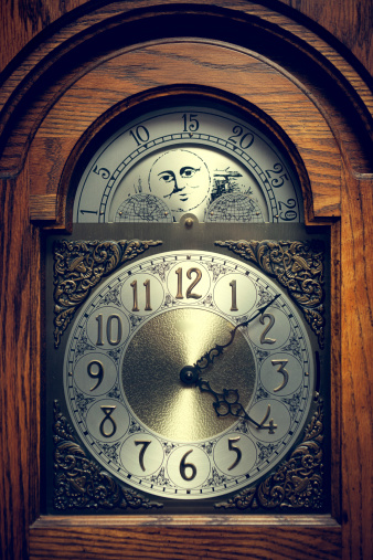 An old fashioned wooden and metal clock, telling the time at just after 4 o'clock.  Vertical.