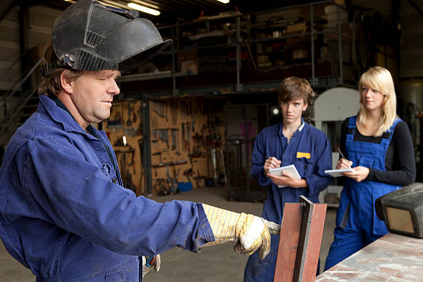 Instructor teaching trainee or worker how to weld metal
