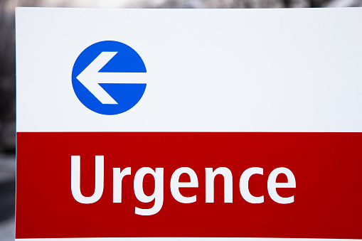 Emergency exterior hospital sign in French with a white arrow surrounded by blue circle on a white background.  This is outside a hospital emergency entrance in Montreal.