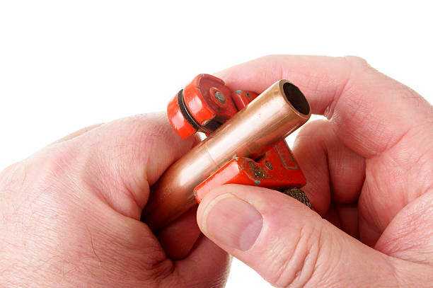 Man's hands cutting 15mm copper tube for plumbing with wheel type pipe cutter.