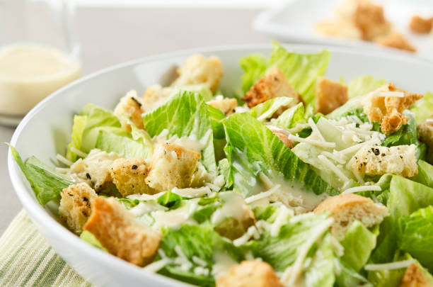 Caesar Salad "SEVERAL MORE IN THIS SERIES. Closeup of a fresh caesar salad, with romaine lettuce hearts, croutons, parmesan cheese and dressing.  Dressing and croutons in background.  Very shallow DOF." augustus caesar photos stock pictures, royalty-free photos & images