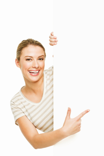 A woman is pointing at a blank wall and smiling towards camera.  Vertical shot. Isolated on White