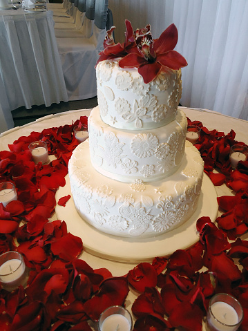 Close up of a wedding cake at a wedding surrounded by candles and rose petals.  More wedding images